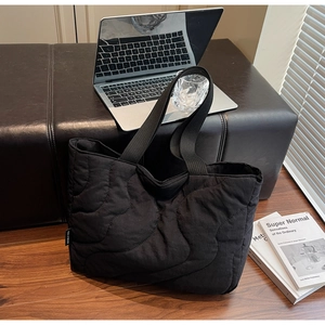Detail of black wave quilted puffer tote bag on a bench with office accessories