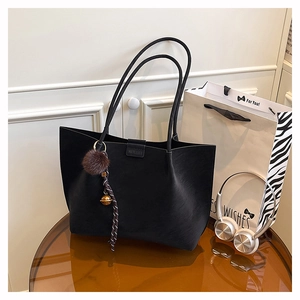 Detail of a black matte tote bag with a plush charm on a glass table in a modern setting