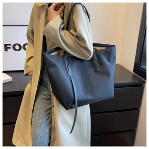 Détail d'un grand sac fourre-tout noir sur un mannequin en trench-coat montrant la taille