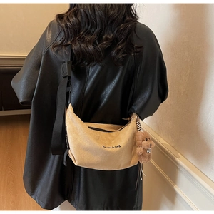 Detail view of khaki suede crossbody bag with bear pendant and black shoulder strap