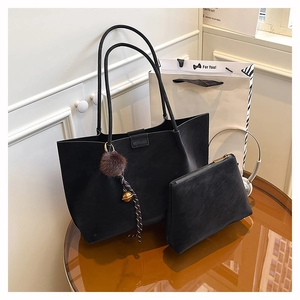 Detail of black matte tote bag set with plush charm and pouch on amber desktop