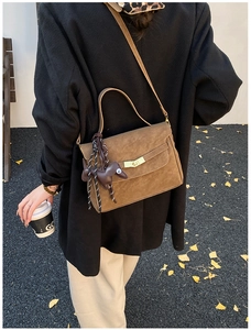 Outdoor shot of a brown suede shoulder bag featuring a cute dog charm and golden clasp