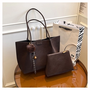 Close-up of deep brown suede tote bag set with bell charm on amber glass table