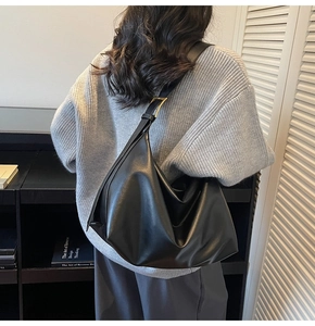 Detail of black leather hobo bag with gold metal buckle on shoulder strap and soft folds