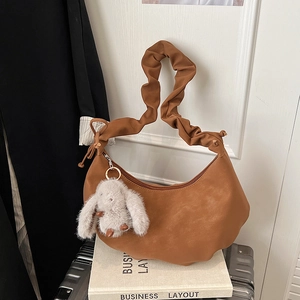 Detail view of brown pleated shoulder bag with matte leather finish and white rabbit charm
