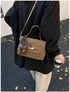 Detail of a brown matte shoulder bag with a cute dog charm styled in an autumn setting