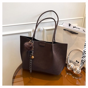 Detail of dark brown leather tote bag featuring a decorative pompom and brand embossing