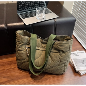 Detail of army green quilted tote bag with wave texture and front zipper pocket on wood floor