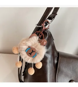 Detail of a brown plush bear charm with poms and a bell on a leather tote bag
