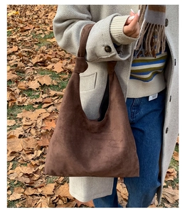 Close-up of a brown suede hobo bag with a knotted handle on autumn leaves