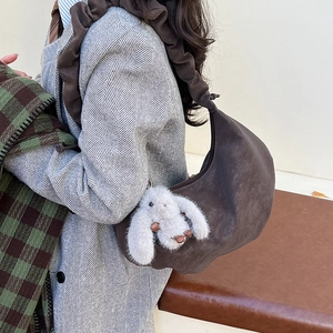 Detail of dark brown crescent bag with pleated strap and white bunny plush charm