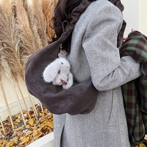 Detail of dark brown crescent shoulder bag with pleated strap and rabbit pendant