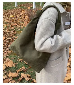 Detail of dark green suede hobo bag with knotted strap shown on an autumn coat