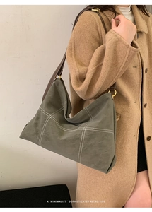 Detail of grey-green hobo bag featuring white cross-stitching and brown leather strap
