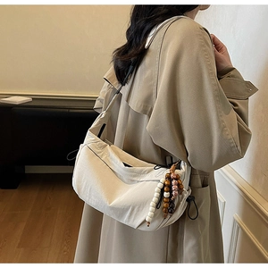 Detail of white nylon crossbody bag featuring side drawstring and wooden bead charm