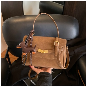 Detail of a brown suede crossbody bag with gold buckle and cute dachshund dog charm