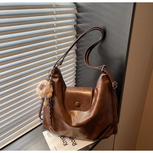 Detail of a brown half-moon crossbody bag with a round buckle and lion pendant