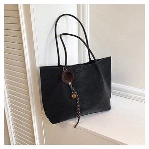 Detail of black textured tote bag featuring a leather brand tag and plush pompom charm