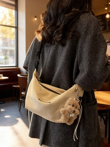 Beige canvas crescent shoulder bag with bear pendant and black adjustable strap