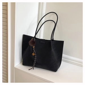 Detail shot of the matte black tote bag featuring a brand logo and a fuzzy pompom charm