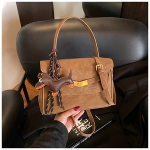 Detail of a brown suede crossbody bag featuring a leather dachshund dog charm and gold buckle
