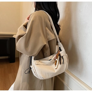 Detail of cream nylon crossbody bag with ethnic wood bead charm and wide shoulder strap