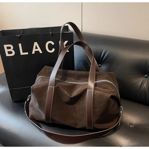 Detail of dark brown suede travel bag with smooth leather straps on a black bench