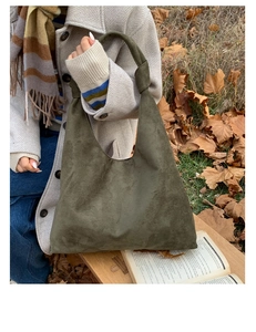 Close-up of dark green suede tote bag featuring unique knotted handles in an autumn setting