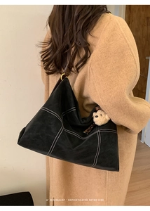 Detail of minimalist tote bag with contrast stitching and plush bear charm accent