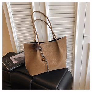 Detail view of brown large tote bag with fuzzy ball charm and woven cord on white shutters