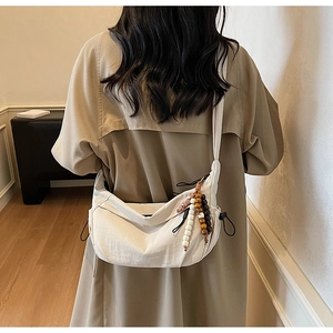 Detail of beige nylon crescent bag featuring a ethnic style wooden bead charm on strap