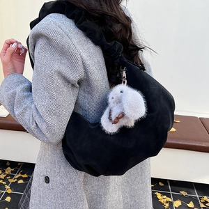 Detail of black crescent shoulder bag with pleated strap and rabbit charm on wool coat