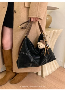Detail of black hobo bag with contrast stitching, brown leather strap and bear charm