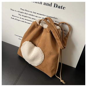 Detail view of brown suede tote bag featuring white faux shearling heart and drawstring