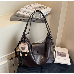 Close-up of a dark brown large hobo bag with a cute plush bear charm on a bench