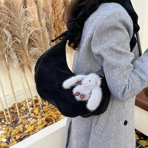 Detail of black crescent shoulder bag with pleated strap and rabbit plush pendant in autumn