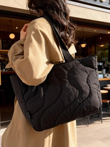 Quilted black puffer tote bag with wave stitching carried by a model in a trench coat