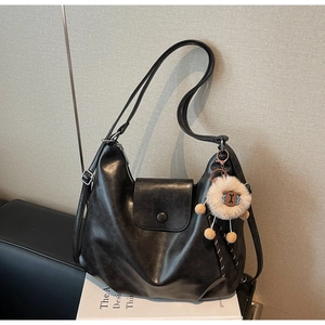 Close-up of black matte leather hobo bag with cute sheep plush pendant and magnetic closure