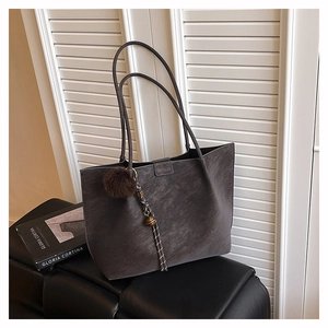 Detail of dark gray suede tote bag featuring a brand logo and a fuzzy pom-pom charm