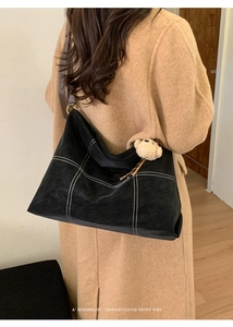 Detail of black tote bag with white stitching, brown strap and plush bear charm