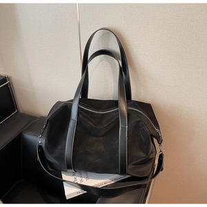 Detail of large black travel bag with white stitching and silver hardware on a leather chair