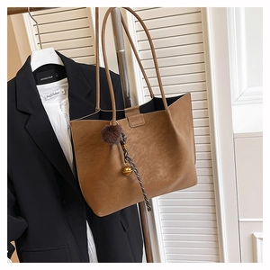 Detail of retro brown tote bag with decorative plush ball and braided lanyard