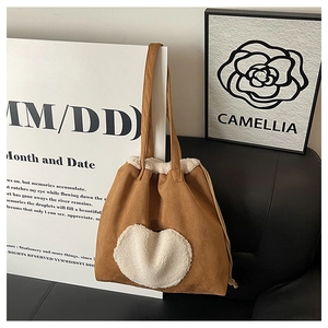 Detail of vintage brown suede tote bag featuring a large white plush heart on leather sofa