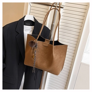 Brown matte tote bag with fuzzy ball charm hanging on a metal rack in a minimal office setting