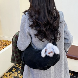 Detail of black suede dumpling bag with plush bunny charm on model in autumn setting