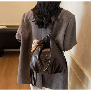 Detail of dark brown pleated crescent bag with high-shine finish and plush charm