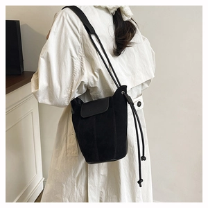 Detail of a black suede bucket bag showing texture contrast and long drawstring decor