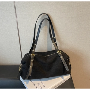 Detail of black suede shoulder bag with adjustable gold eyelet straps on a book
