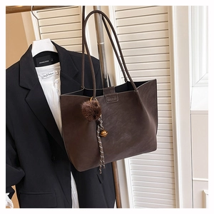 Detail of dark brown suede tote bag with decorative pom-pom and metal bell charm