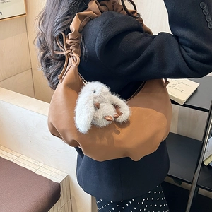 Detail of brown pleated hobo bag featuring a white plush rabbit charm accessory